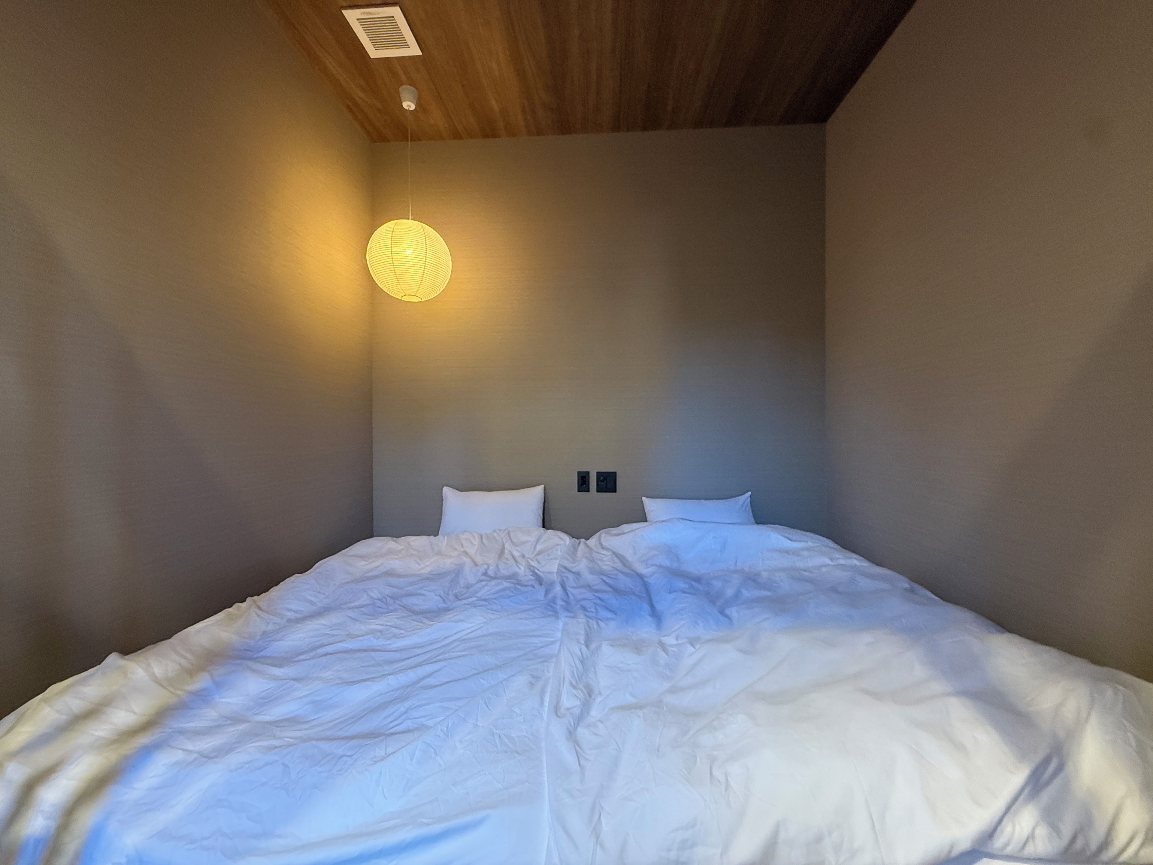 A bedroom with a large bed, a ceiling light fixture, and a wall-mounted air vent.