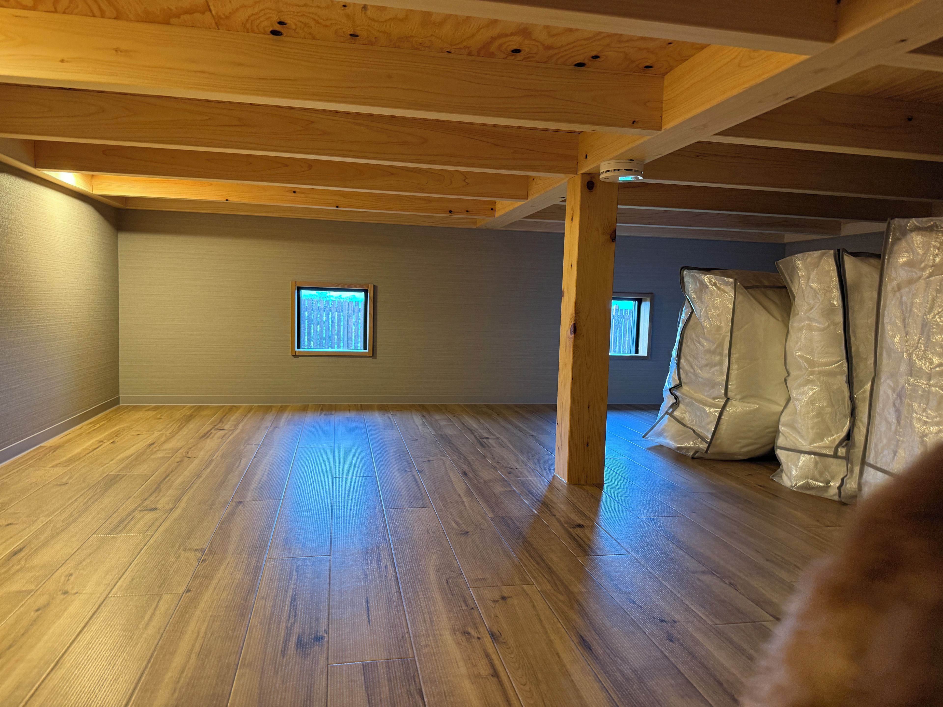 A room with wooden beams, a window, and a corner with insulation materials.