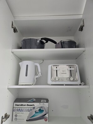 Una cocina con hervidor, tostadora y plancha a vapor en los estantes.