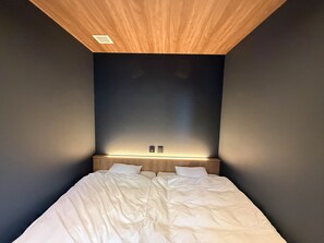 A bedroom with a wooden ceiling, a bed with white bedding, and a wall-mounted light fixture.