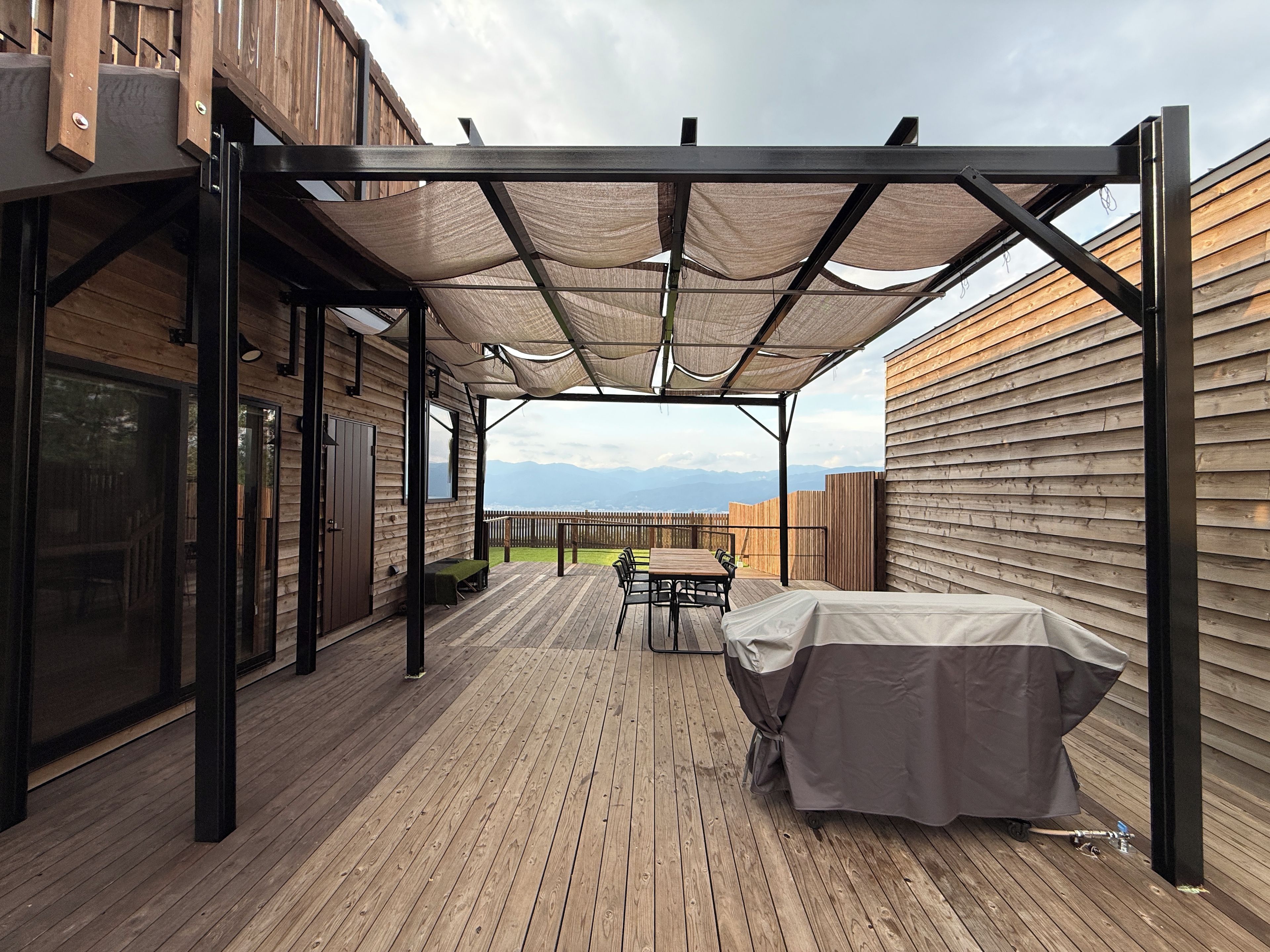 A covered outdoor area with a wooden deck, a table with chairs, and a barbecue grill.