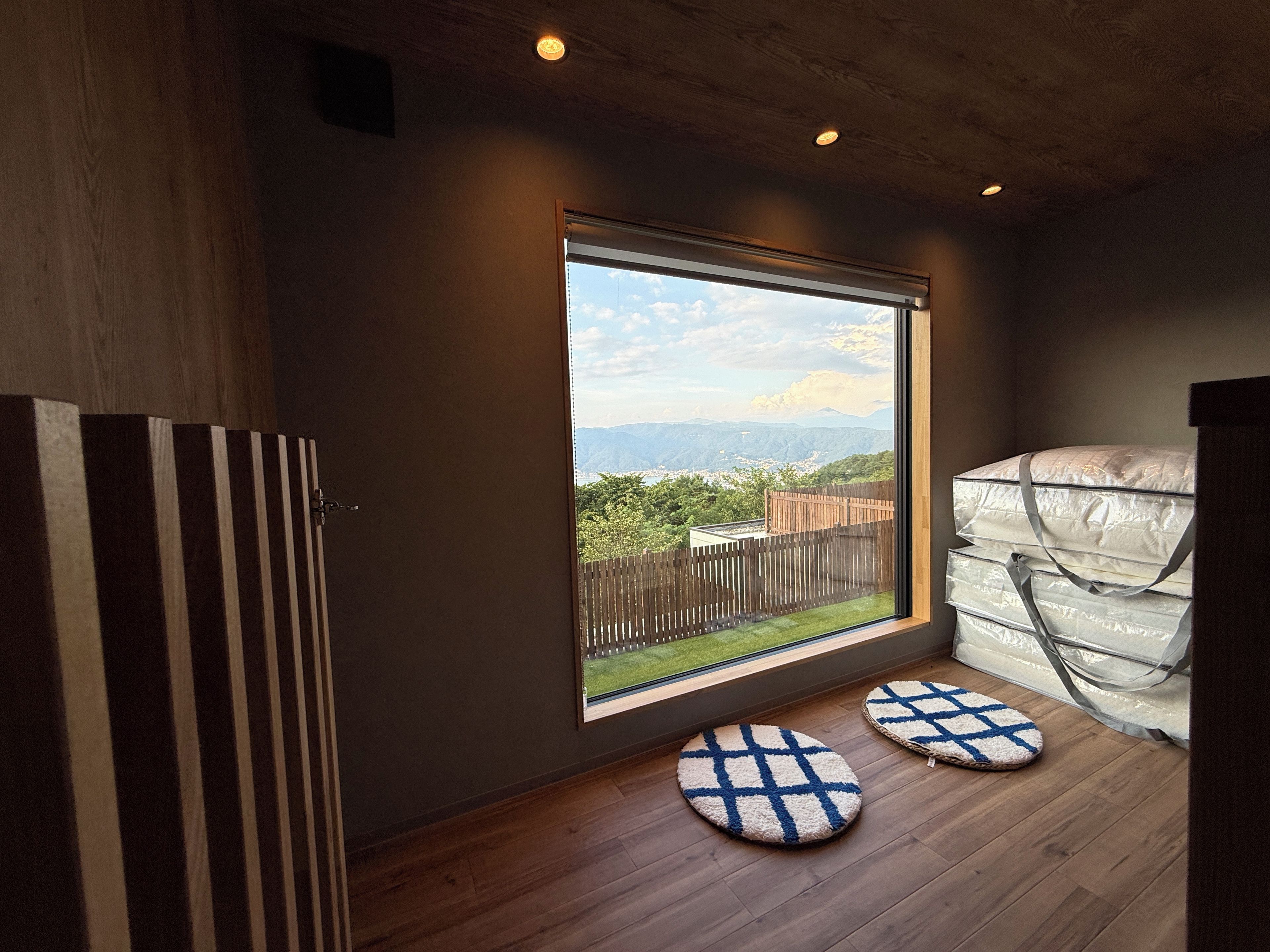 Une pièce dotée d’une grande fenêtre, d’un plancher en bois et de deux tapis ronds.