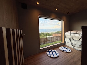 A room with a large window, wooden flooring, and two round rugs.