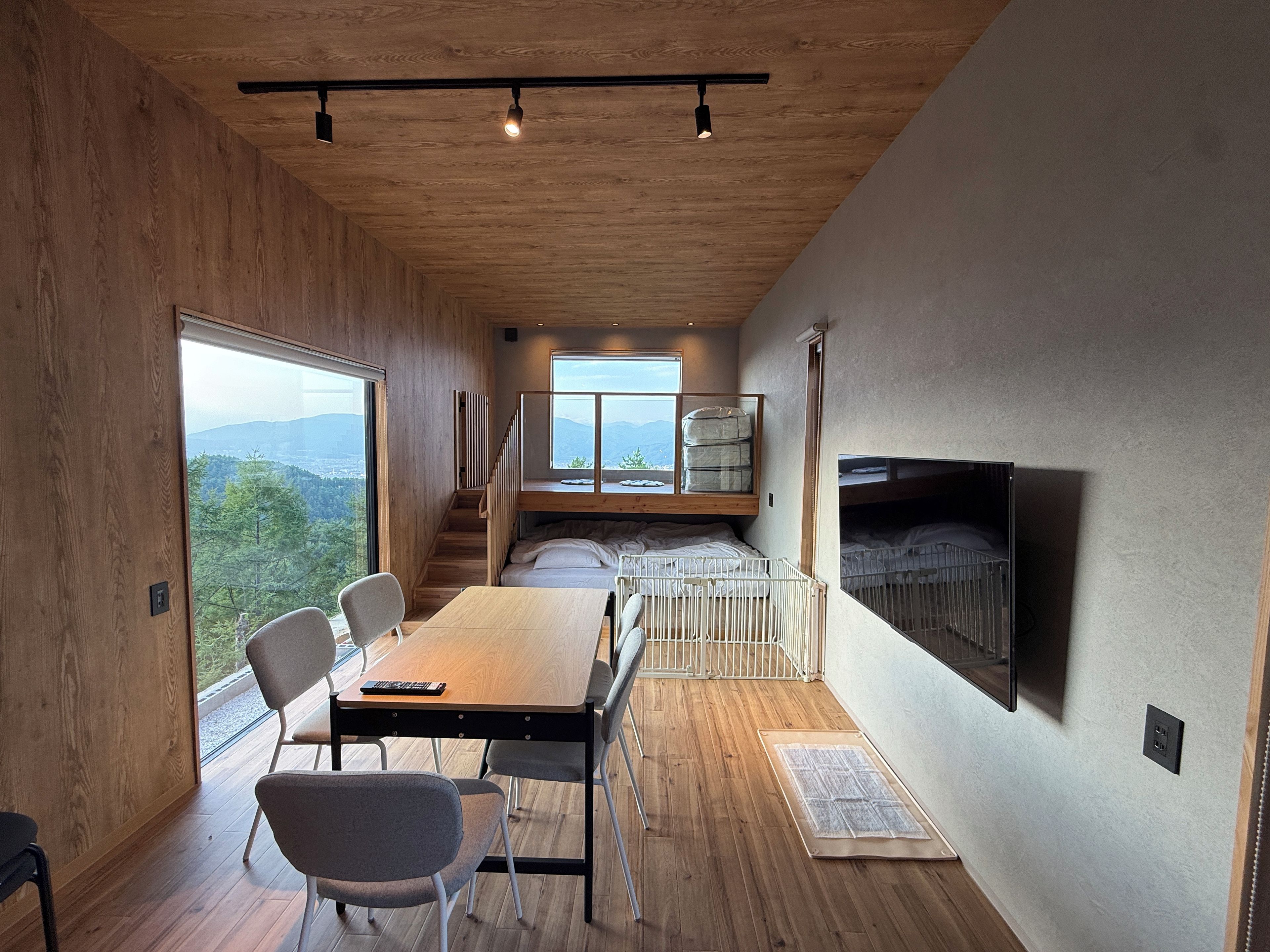 A modern interior with a wooden floor, a dining table with chairs, a fireplace, and a large window offering a view of the outdoors.