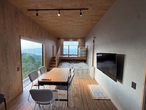 Un intérieur moderne avec un plancher en bois, une table à manger avec des chaises, une cheminée et une grande fenêtre donnant sur l’extérieur.