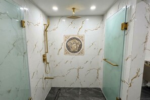 Um banheiro com paredes de mármore, chuveiro com cabeça de chuveiro dourada e um azulejo decorativo com desenho de rosto.