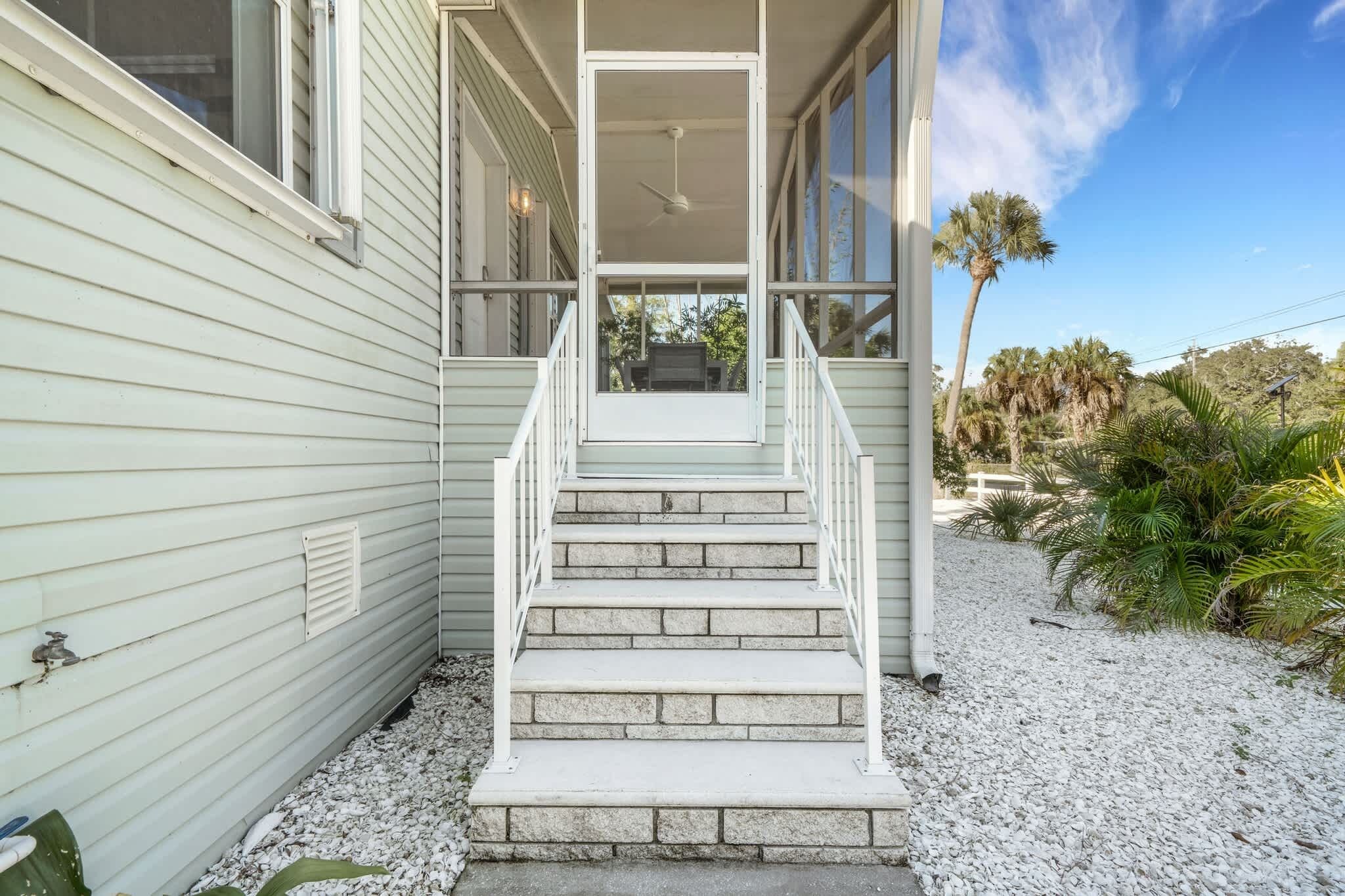 A house with a front porch, a ceiling fan, and a view of palm trees.