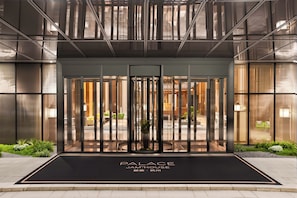 Entrada d'un edifici modern amb una porta de vidre i un felpó negre, amb la indicació 'PALACE JAMHOUSE'.