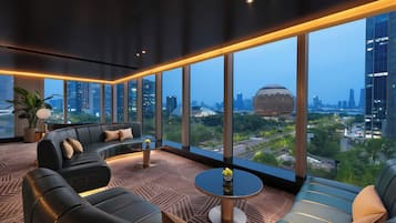 A modern lounge with a sofa, a round table, and large windows offering a city view.