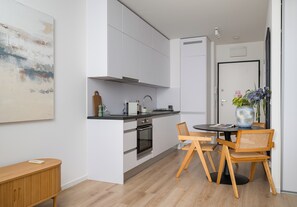 Una cocina moderna con armarios blancos, encimera negra y comedor con mesa redonda y sillas de madera.