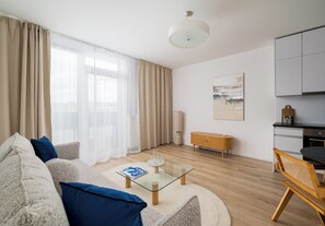 Una sala de estar moderna con una mesa de centro de vidrio, un sofá con cojines, un comedor con una silla y una cocina al fondo.