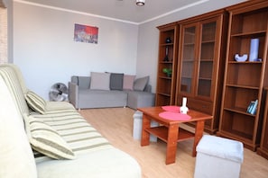 A living room with a sofa, a wooden table with a vase, and a bookshelf. - Głogów Comfort Stay Apartament (Głogów)