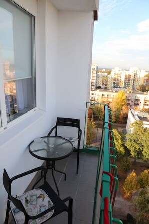 A balcony with a glass table and chairs, a window, and a view of a cityscape. - Głogów Comfort Stay Apartament (Głogów)