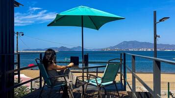 A wooden deck with two chairs and a table, overlooking a beach and the sea.