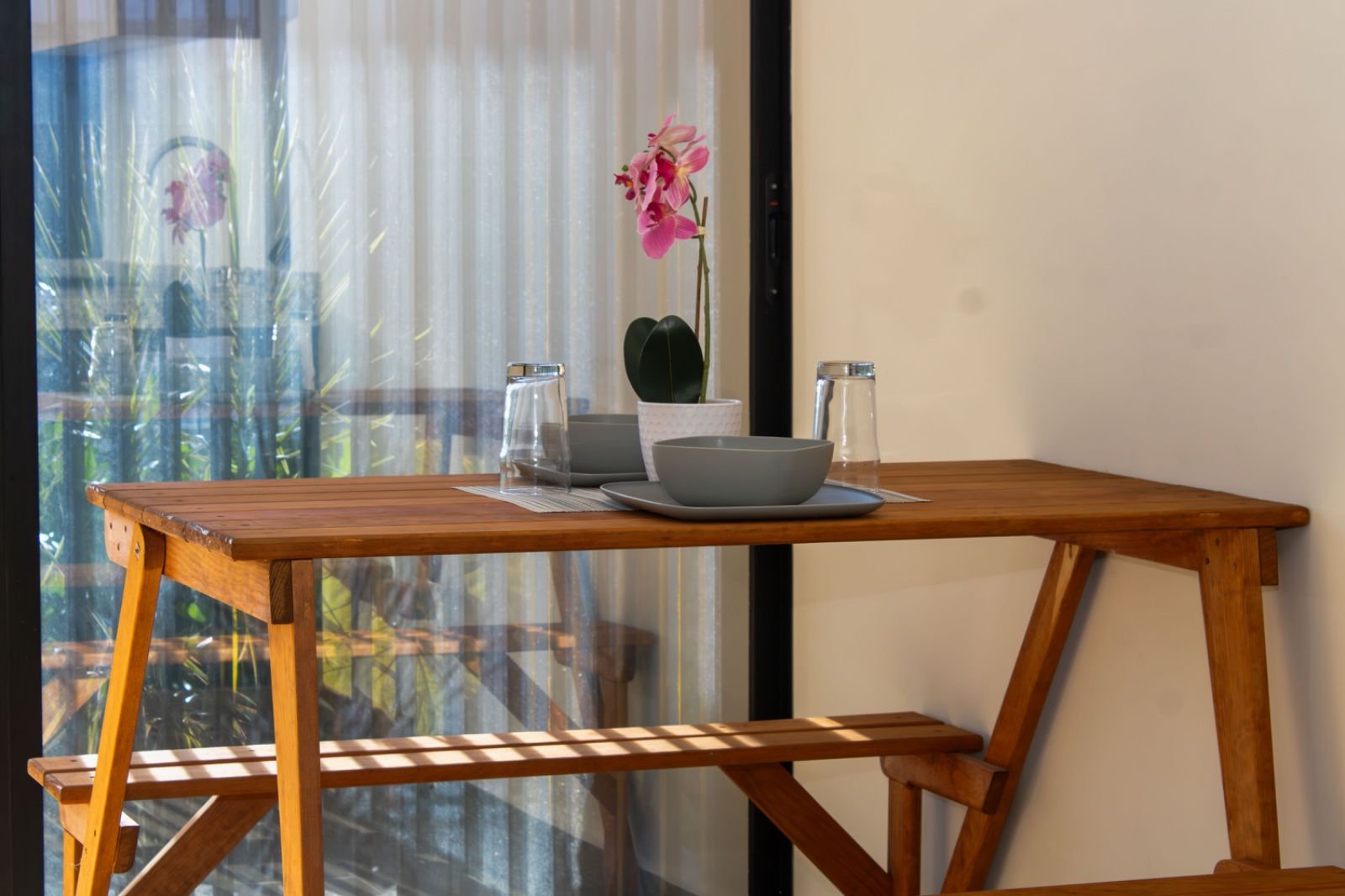Una mesa de madera con un bol, una jarra, una planta en maceta y un vaso de agua sobre un alféizar.