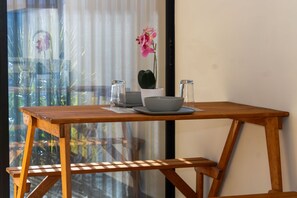 A wooden table with a bowl and a pitcher, a potted plant, and a glass of water on a windowsill.