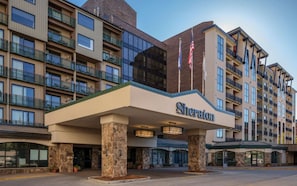 Ein Sheraton Hotel mit moderner Fassade, mehreren Balkonen und einem markanten Eingang mit amerikanischen Flaggen.