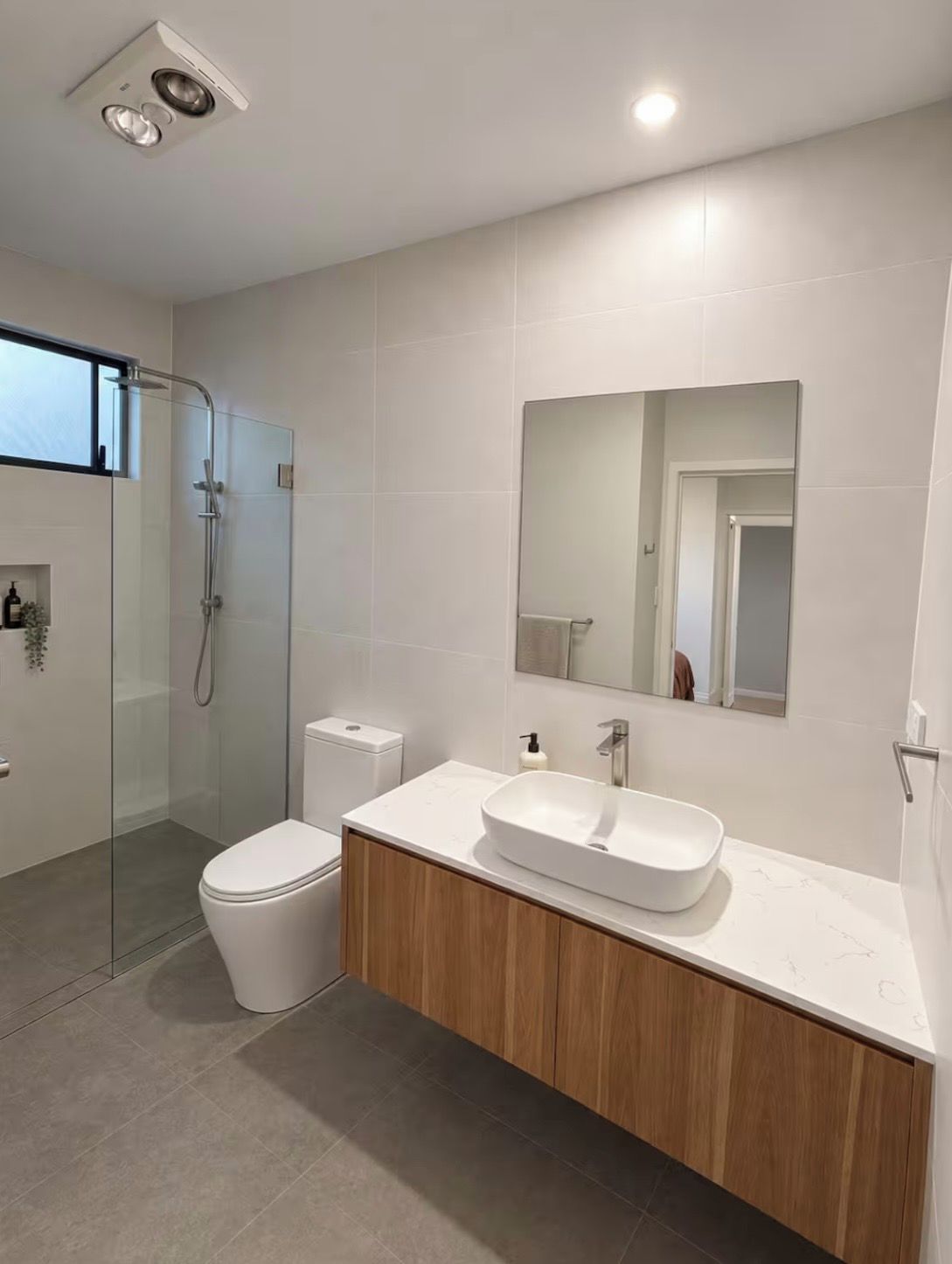 Et moderne badeværelse med et brusebadekar i glas, et hvidt toilet og en vask med spejl.