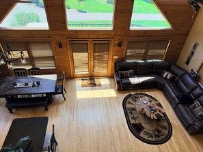 A spacious living area with a large wooden ceiling, a black leather sofa, a dining table with chairs, and a view through the windows. - Hot Tub • Private Pond • 12-Acr Retreat • Sleep 14 (Binghamton)