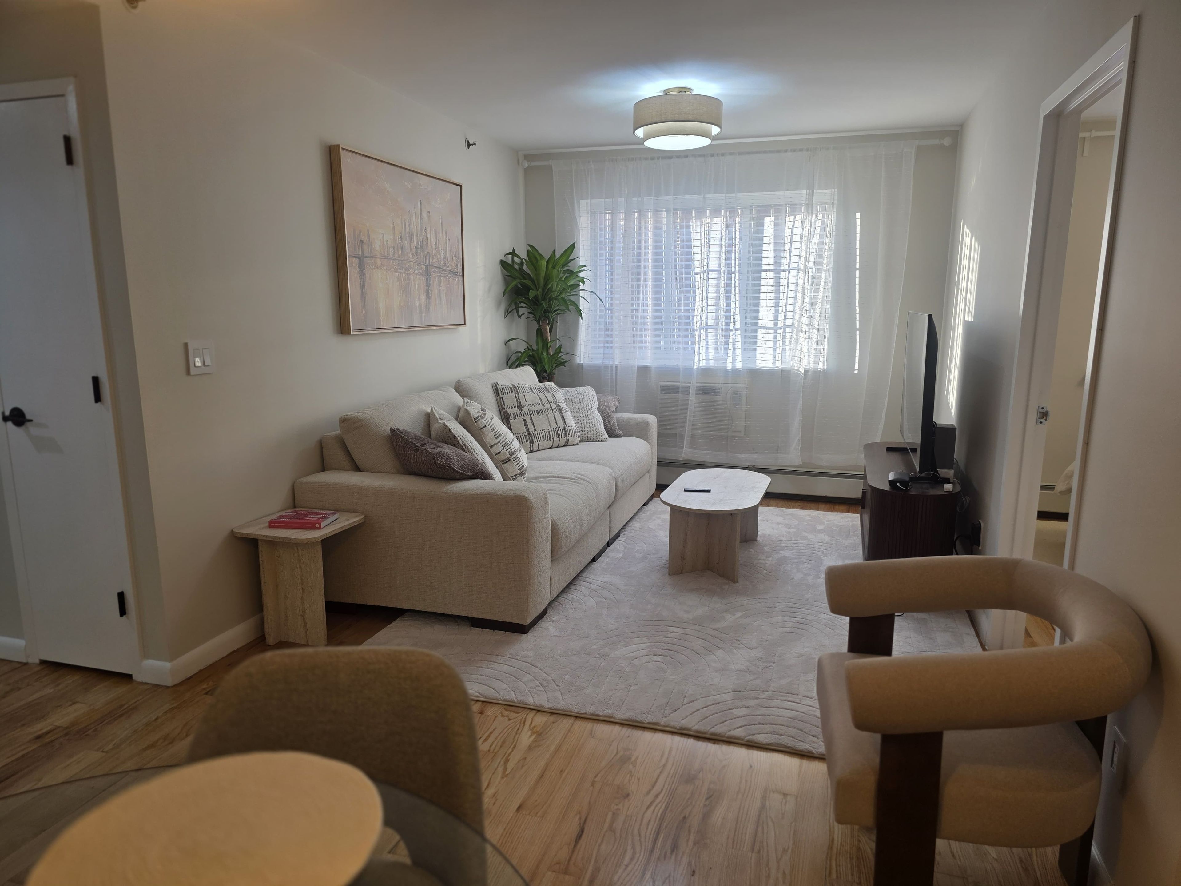 Ein Wohnzimmer mit einer Couch, einem Couchtisch und Sesseln. Ein Fernseher und eine Pflanze sind ebenfalls vorhanden.