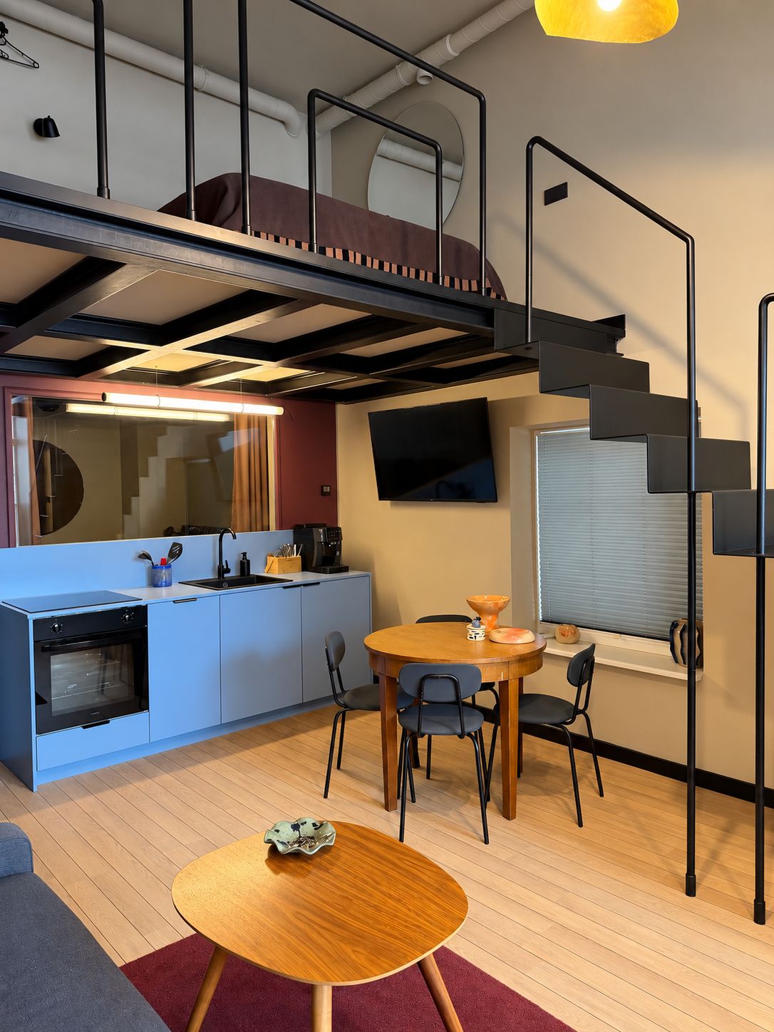 A modern kitchen with a built-in oven, a dining area with a round table, and a staircase leading to an upper level.