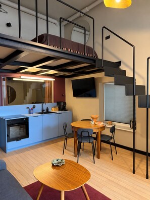 A modern kitchen with a built-in oven, a dining area with a round table, and a staircase leading to an upper level. - G Loft – Spacious Apartment with Bathtub & Private Entrance (Kaunas)