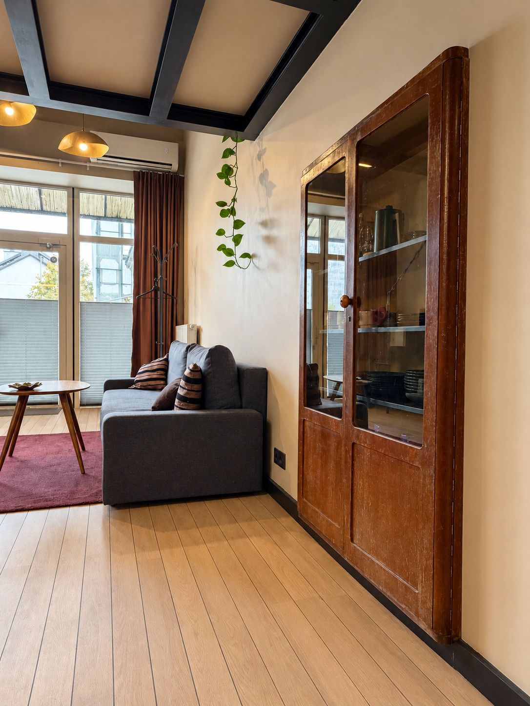 A modern living room with a grey sofa, wooden floor, and a large wooden cabinet with glass doors.