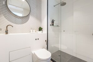 Un baño moderno con un lavamanos blanco, un espejo redondo, cabina de ducha con mampara de cristal y un inodoro.