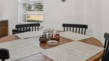 Une table de salle à manger ronde, accompagnée de quatre chaises, une fenêtre avec des stores et un porte-ustensiles fixé au mur.