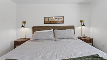 Une chambre à coucher avec un lit, deux tables de chevet, deux lampes, un tableau encadré au mur et une couverture verte sur le lit.
