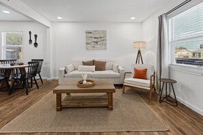 A modern living room with a sofa, coffee table, and a dining area with chairs and a table. - Polk Street Station - 3BR Home Near Downtown Amarillo (Amarillo)