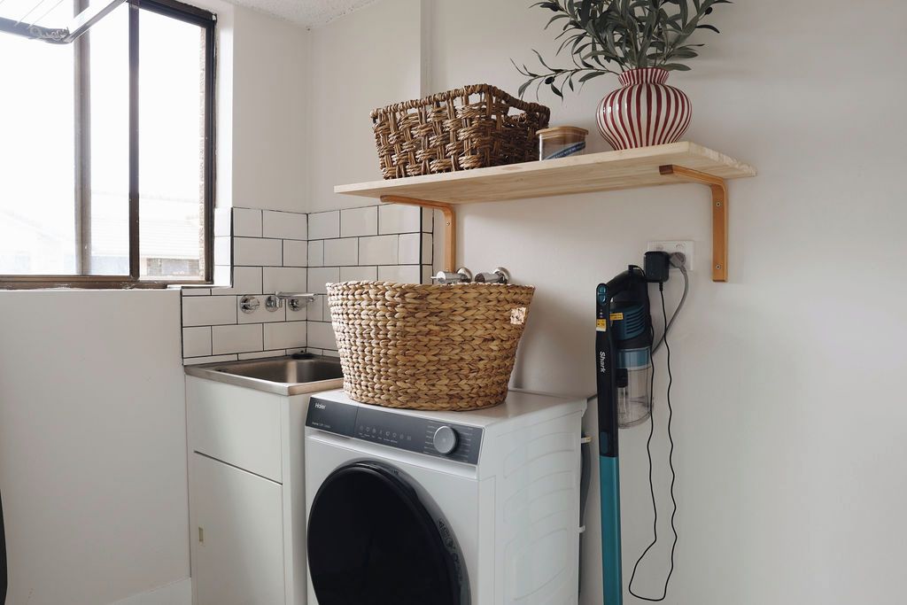 Un espace buanderie comprenant un lave-linge, un panier à linge et une étagère avec une plante.