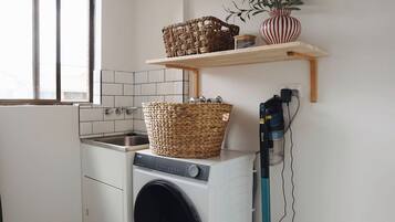 Un espace buanderie comprenant un lave-linge, un panier à linge et une étagère avec une plante.