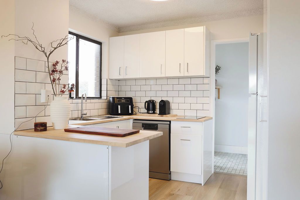Une cuisine moderne avec des meubles blancs, un lave-vaisselle, une machine à café et une fenêtre.