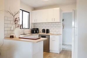 Una cocina moderna con armarios blancos, lavavajillas, cafetera y ventana.