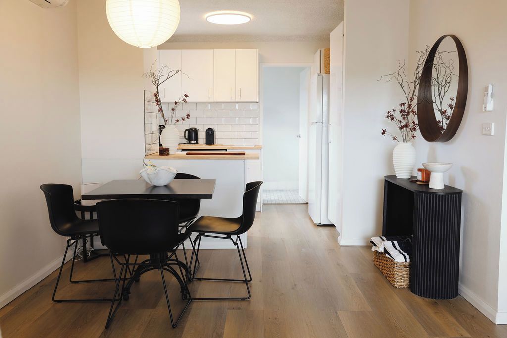 Une cuisine moderne avec des meubles blancs, un plan de travail en bois et un coin repas comprenant une table et des chaises.