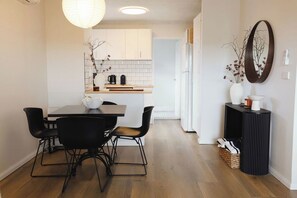 Cocina moderna con armarios blancos, encimera de madera y zona de comedor con mesa y sillas.