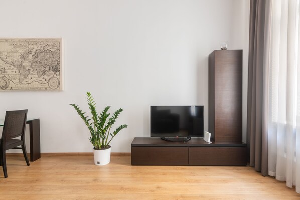 Una sala moderna con un televisor de pantalla plana sobre un mueble de madera oscura, una planta en maceta, un mapa en la pared y un sillón.