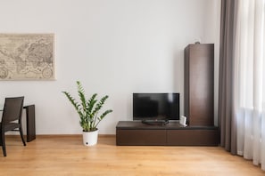 A modern living room with a flat-screen TV on a dark wooden cabinet, a potted plant, a map on the wall, and a chair. - 2 Bedroom Apartment Sleeps 4 - Free Parking (Praha 2)