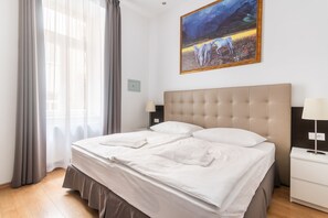 Una camera d'albergo con un letto grande, un comodino, una lampada, un quadro appeso al muro e una finestra con tende.