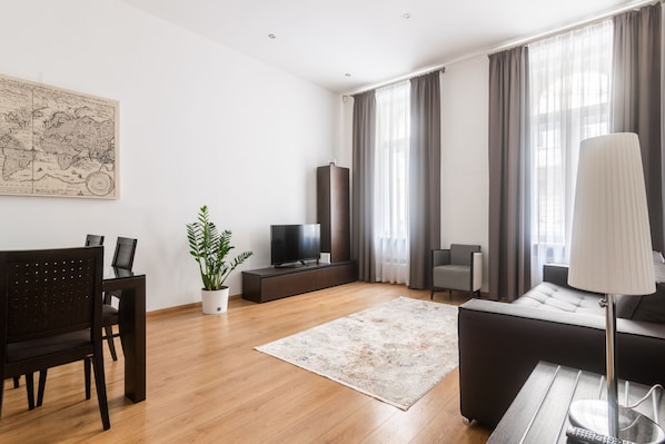 A modern living room with a wooden floor, a dark sofa, a TV, a plant, and a map on the wall. - 2 Bedroom Apartment Sleeps 4 - Free Parking (Praha 2)