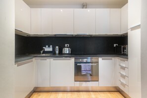 Una cocina compacta con armarios blancos, encimera negra, electrodomésticos de acero inoxidable y suelo de madera.
