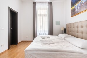 Una habitación de hotel con una cama, una mesita de noche, una lámpara, un cuadro y una ventana con cortinas.