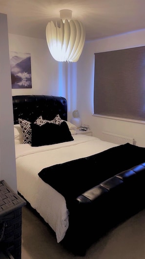 Ett modernt sovrum med en stor säng, en unik taklampa och en tavla som föreställer ett berglandskap.