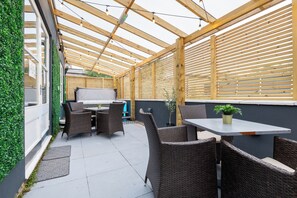 Eine Terrasse im Freien mit einer Holz-Pergola, Korbmöbeln und einem Tisch.