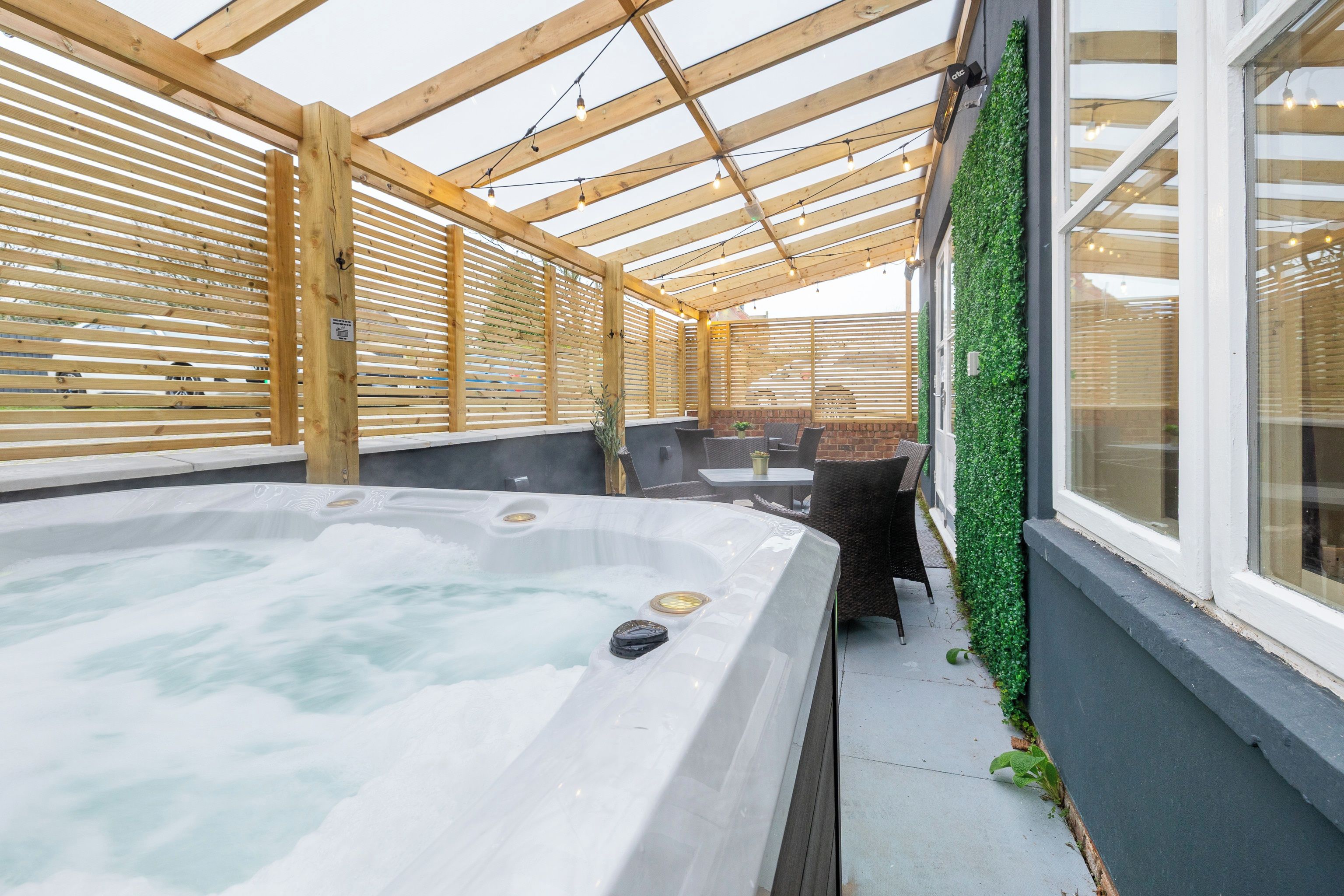 A hot tub area with wooden beams, a glass wall, and a green wall with plants.