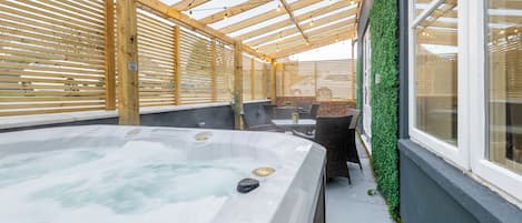 A hot tub area with wooden beams, a glass wall, and a green wall with plants.