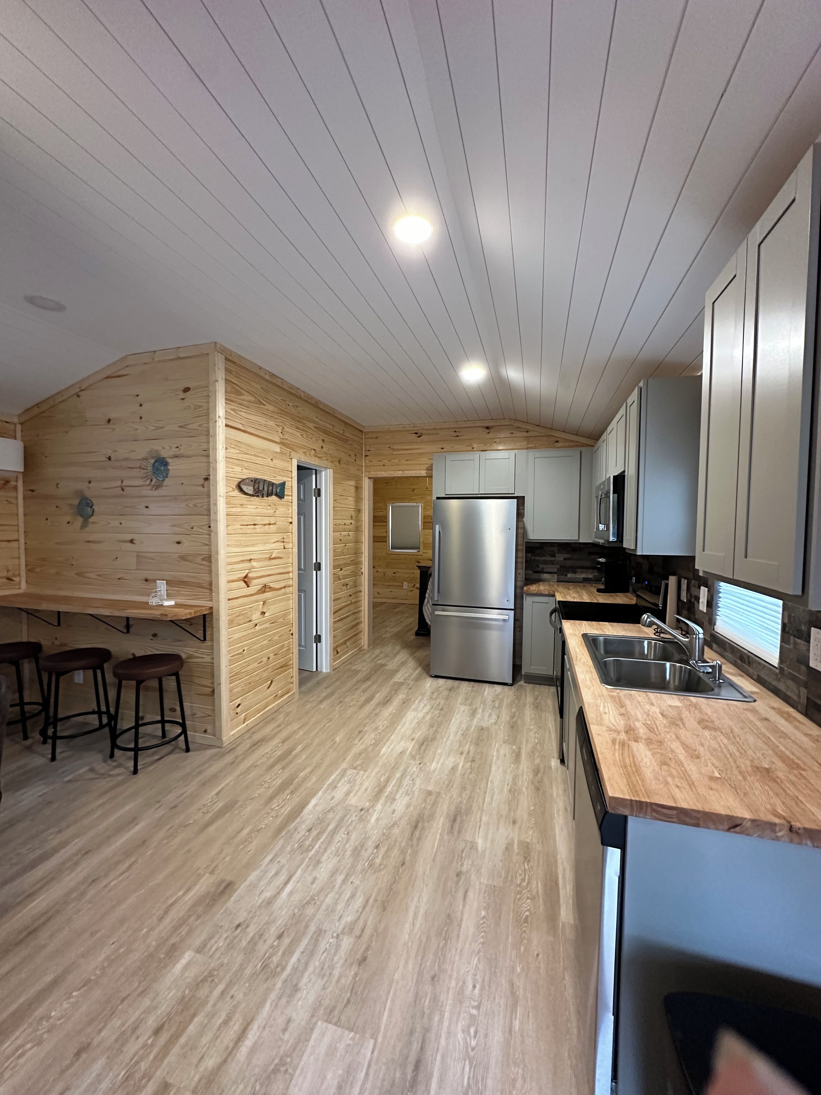 Eine moderne Küche mit Holzwänden, einem Edelstahl-Kühlschrank, einer Spüle und Barhocker.