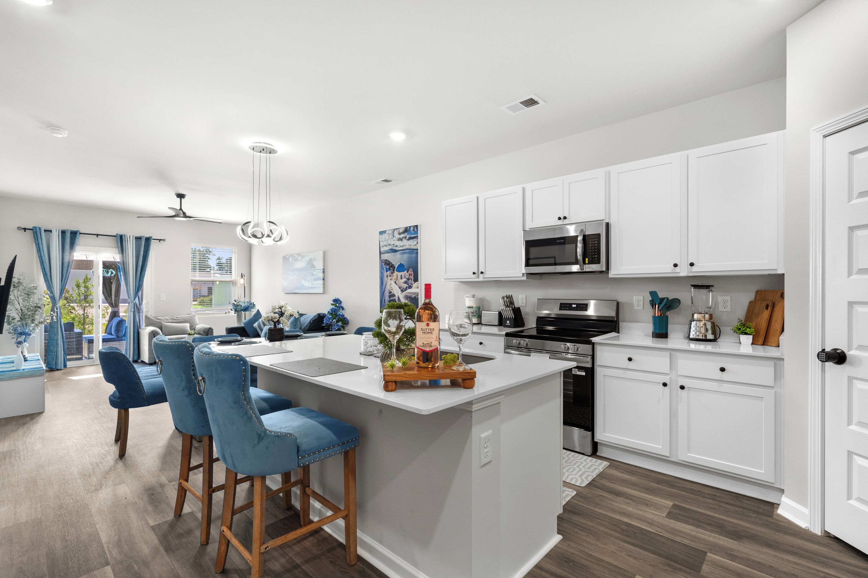 A modern kitchen with white cabinetry, a central island with bar stools, a built-in microwave, and a stainless steel oven.