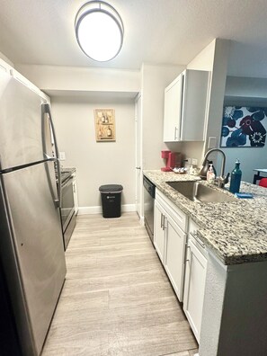 A compact kitchen with a stainless steel refrigerator, a dishwasher, and a granite countertop. - 2-bedroom apartment in beautiful Houston with AC and fitness room (Houston)